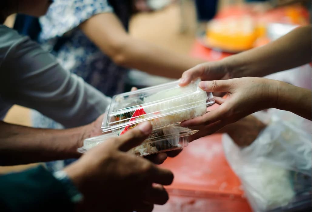 A volunteer hands a prepared meal to a neighbor at an Ihsan Initiative distribution